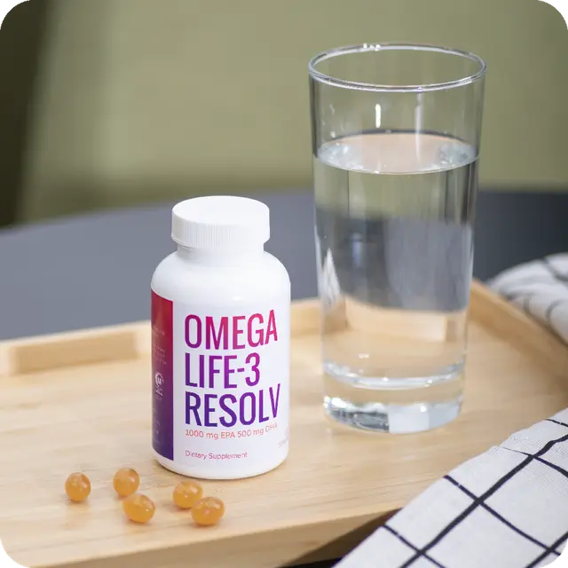 Botella de OmegaLife-3 Resolv junto a cápsulas blandas y un vaso de agua